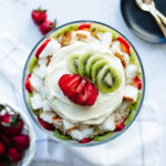 stacked strawberry and kiwi slices on top of cool whip and pudding in a trifle bowl.