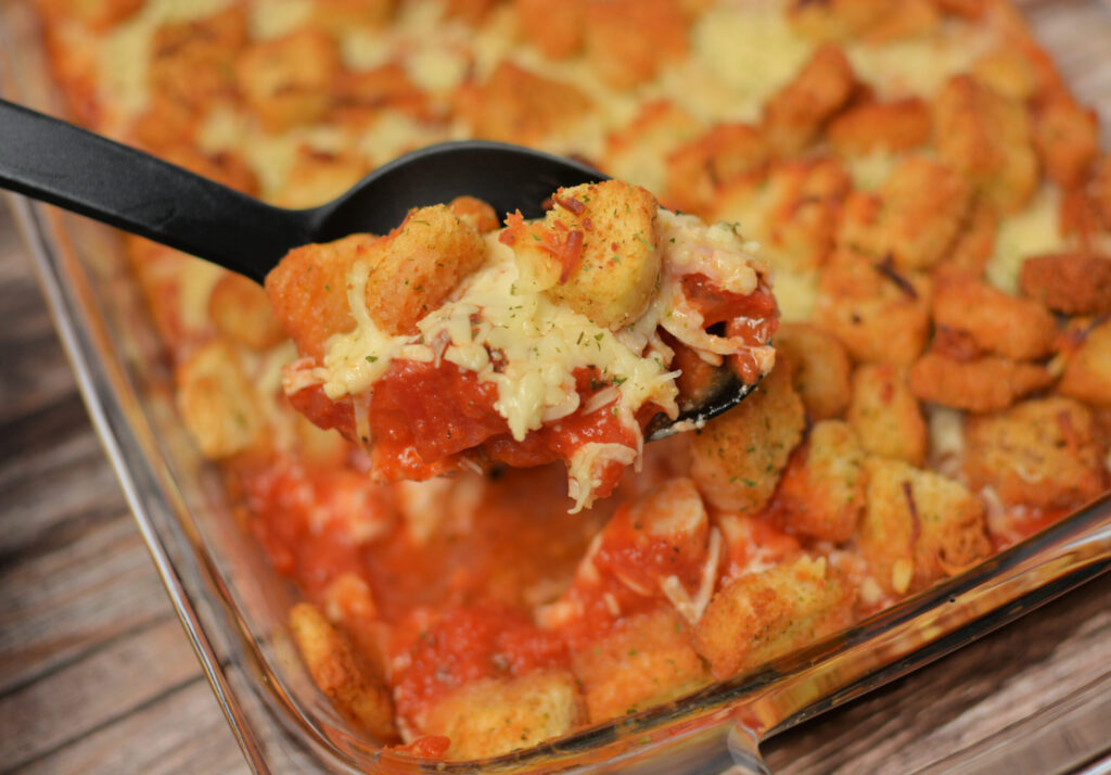 a spoon taking a scoop out of baked chicken parmesan casserole.