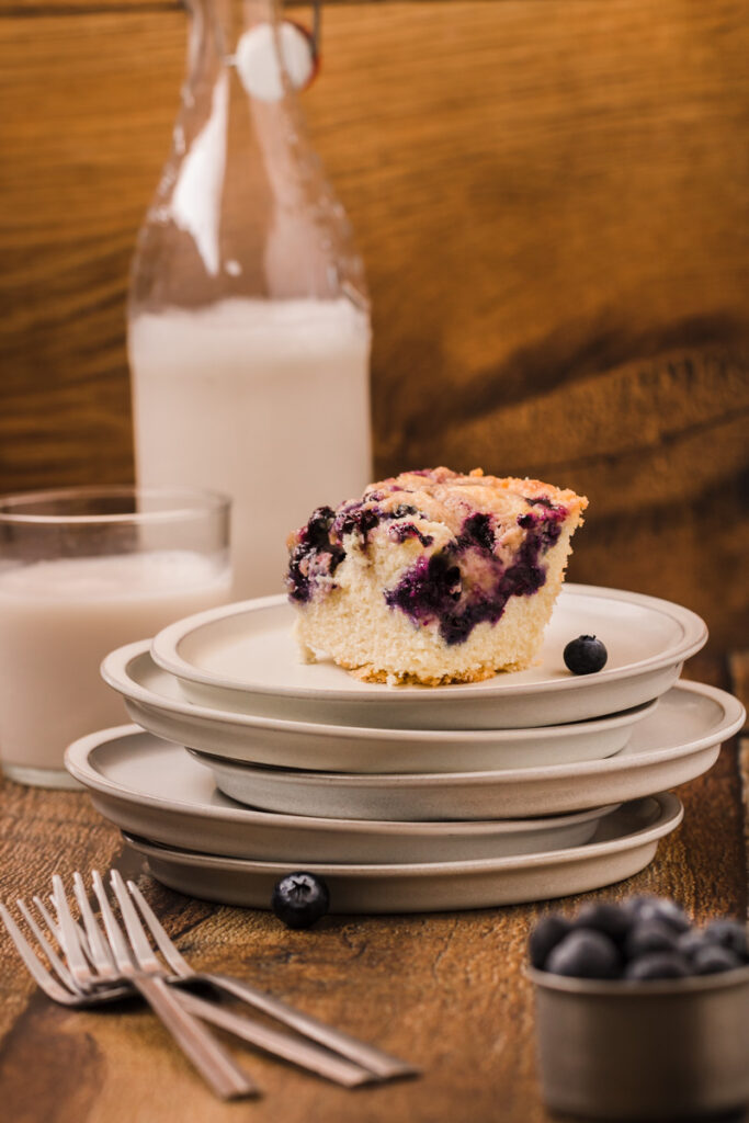 a piece of blueberry buckle on a plate with a glass of milk