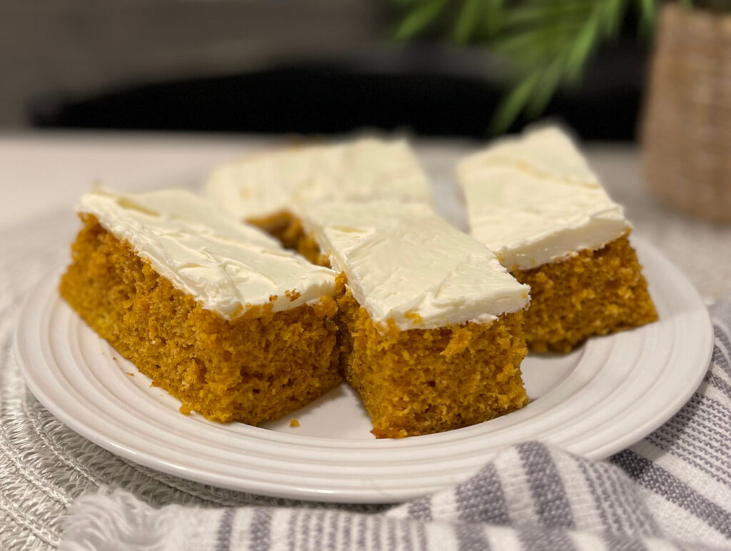 cut pumpkin bars topped with cream cheese frosting and served on a plate