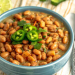 flavor packed charro beans in a bowl with jalapenos on top.