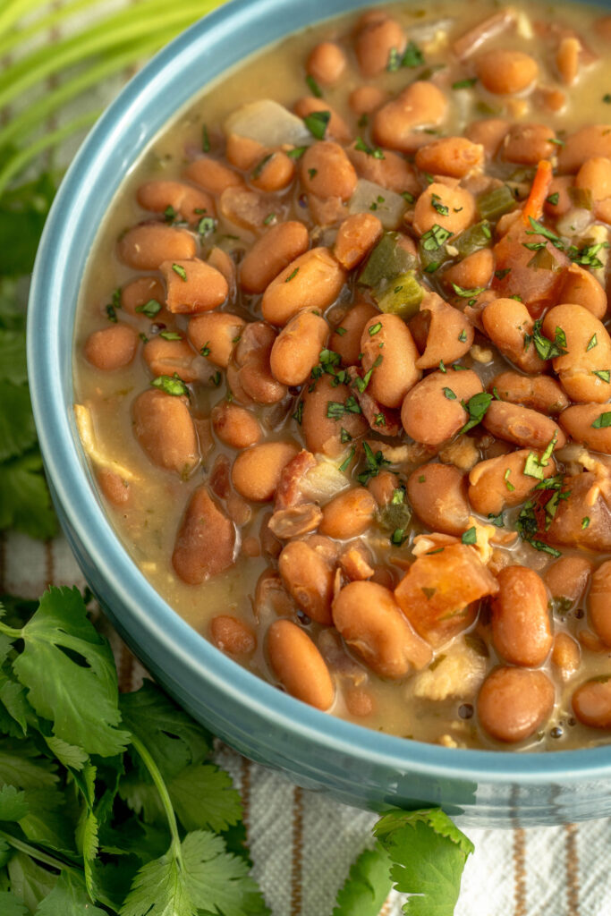 an up close look at Mexican beans in a bowl with spices, pinto beans, bacon, and tomatoes.