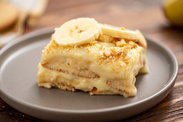 A slice of banana pudding dessert layered with vanilla custard, banana slices, and crushed cookies on a gray plate.