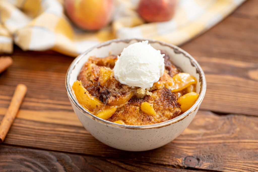 a scoop of peach cobbler served in a bowl with vanilla ice cream
