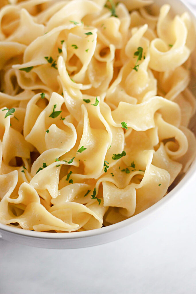 tender buttered Amish noodles in a white serving bowl.