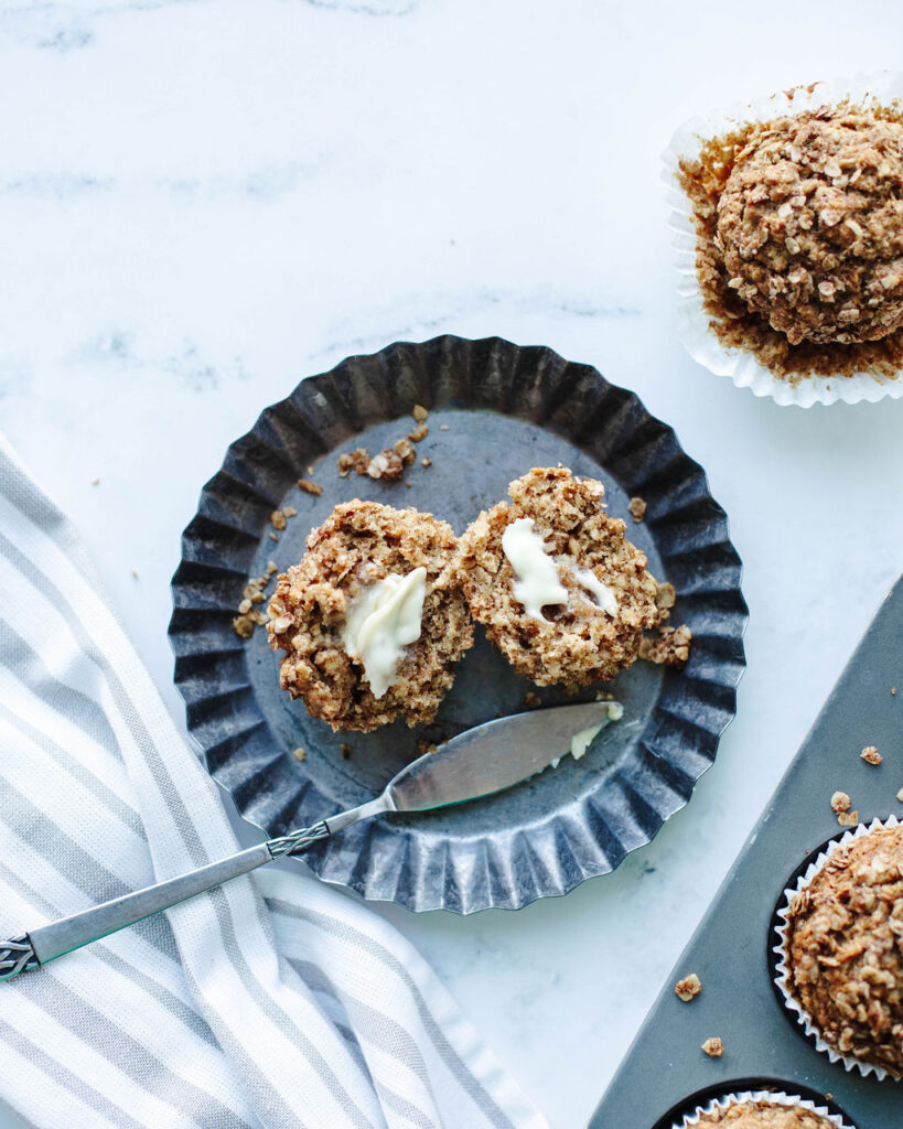 Applesauce Cinnamon Oat Muffins served on a black plate with some butter and a fork.
