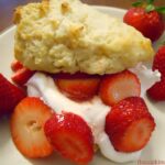 fresh strawberries piled on top of homemade biscuits with whipped cream for a strawberry shortcake dessert