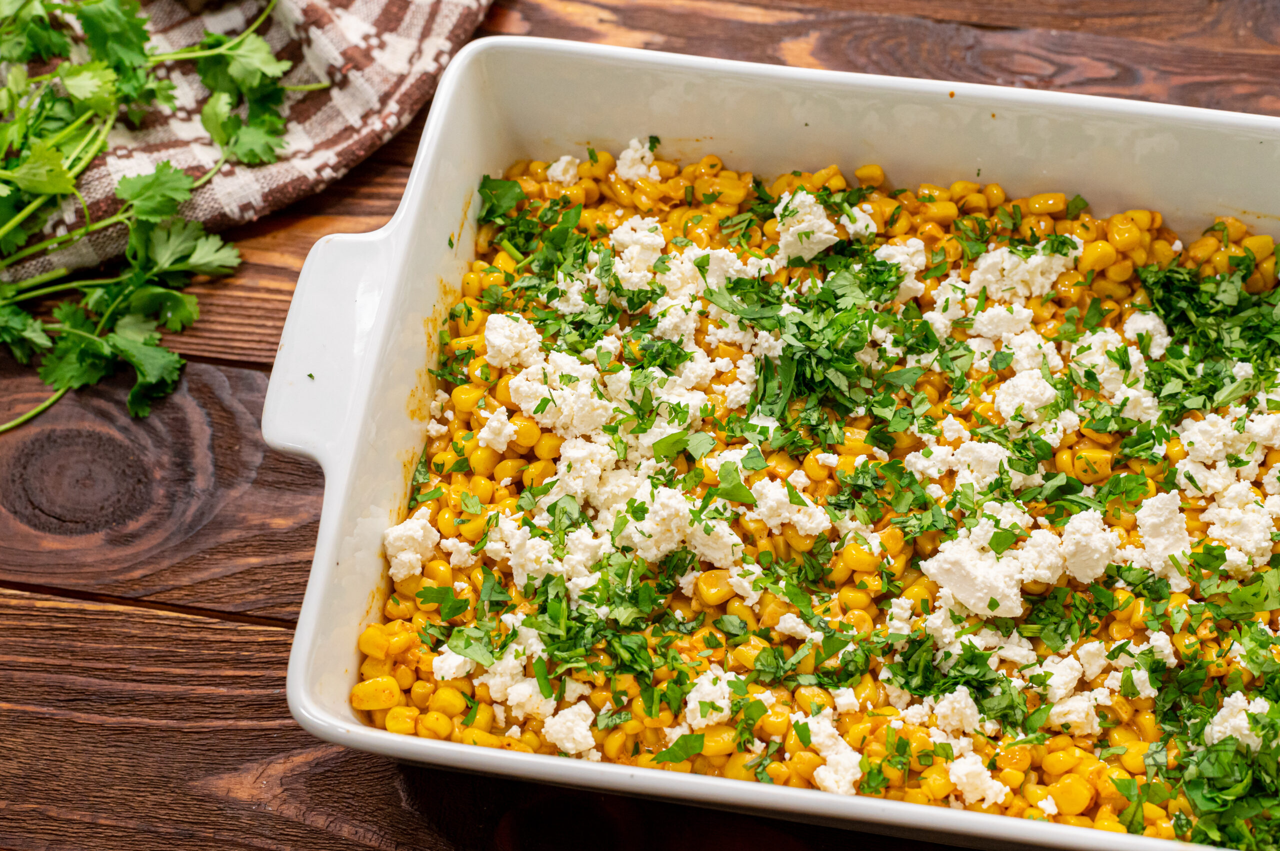 a casserole dish of Mexican corn coated in seasonings, cheeses, and cilantro.