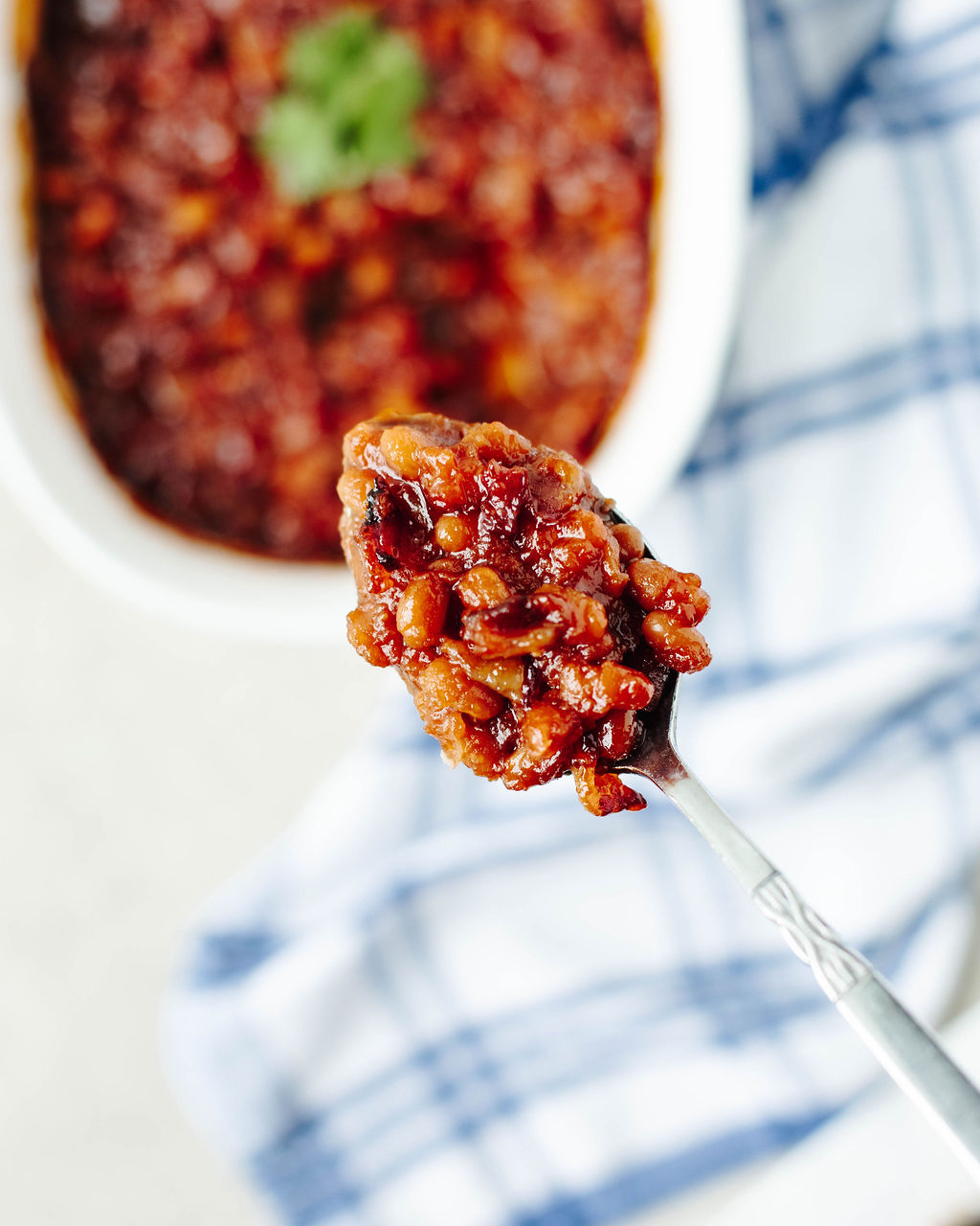 Spoonful of baked beans with bacon on white plate.