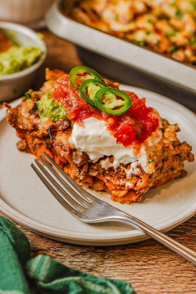 a piece of Taco Bake on a plate with sour cream, tomatoes, and jalapenos.
