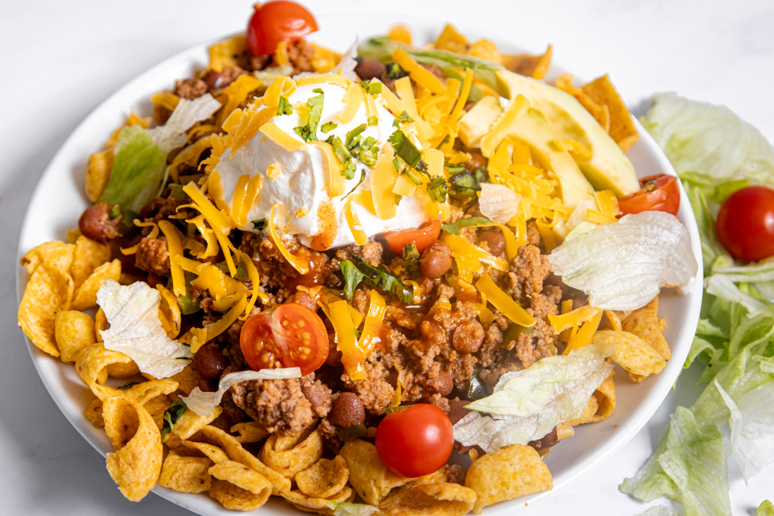 a white plate loaded with corn chips, ground beef, and toppings.