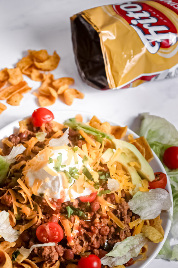 Frito corn chips with a seasoned beef mixture and taco toppings piled on top.