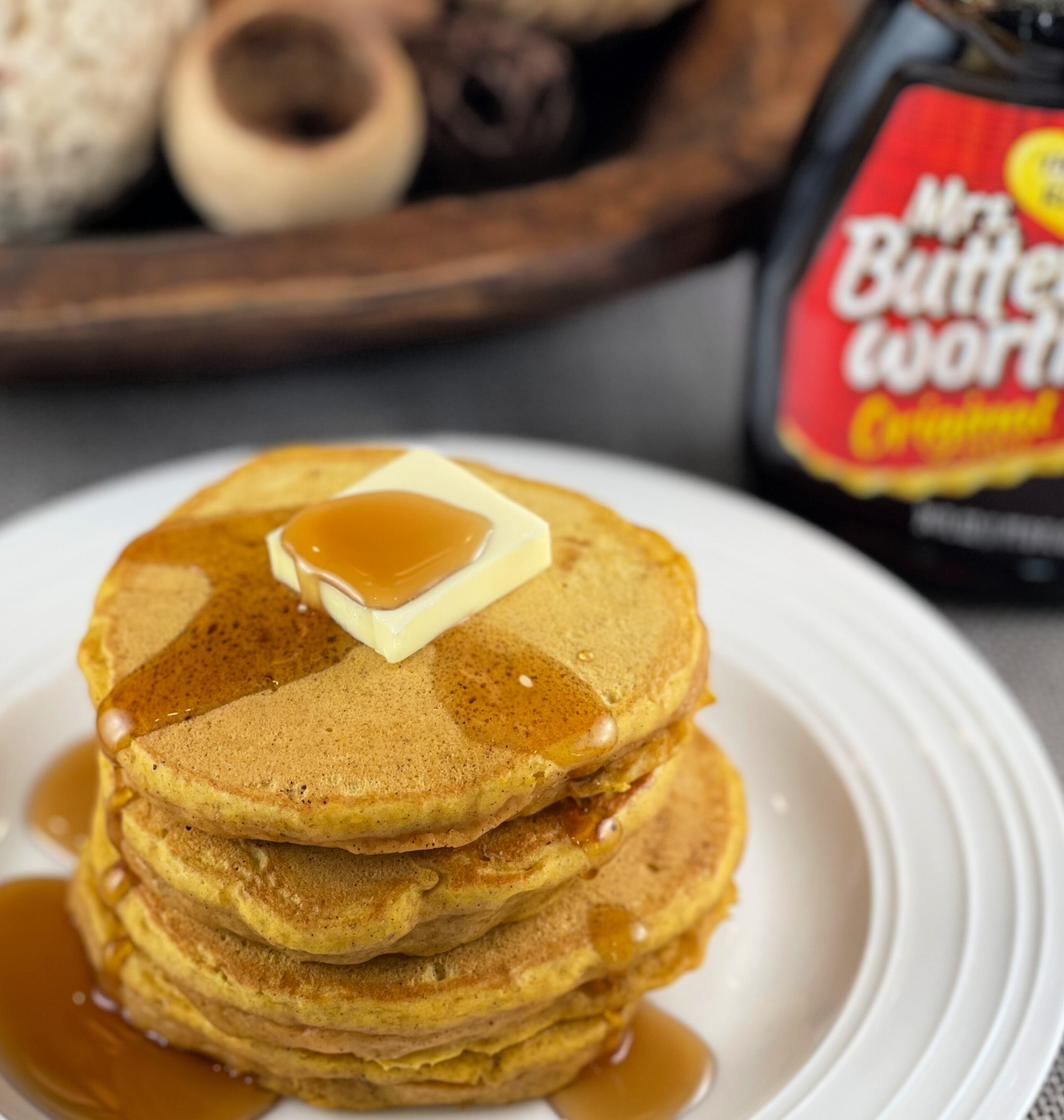 a stack of pumpkin pancakes on a white plate with syrup.