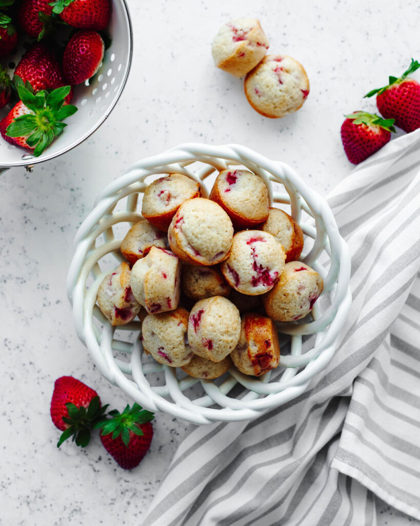 a white decorative bowl with muffins inside.
