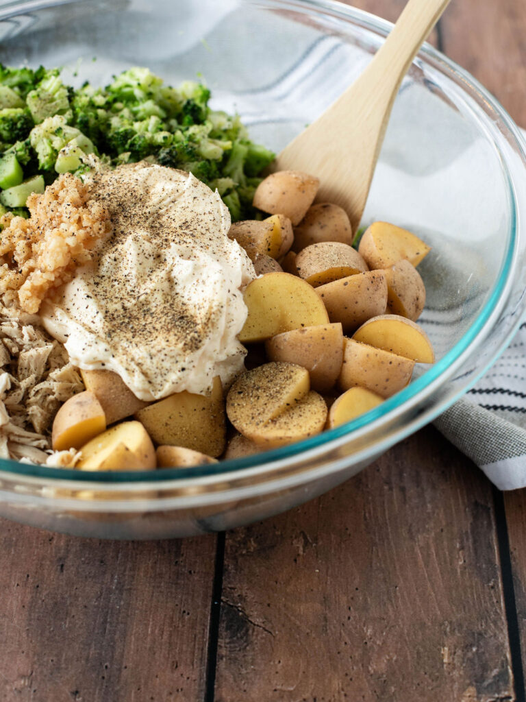 a mixing bowl full of chicken, potatoes, and broccoli with mayonnaise.