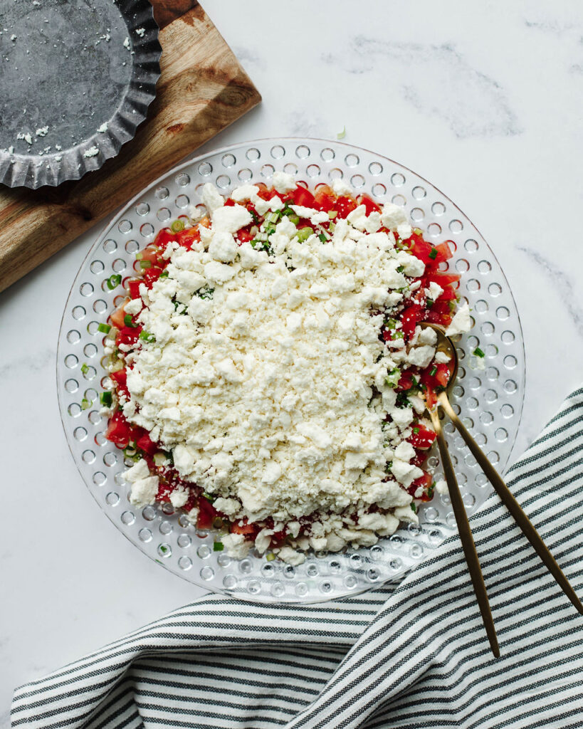 crumbled feta cheese with diced tomatoes and green onions in a glass bowl.