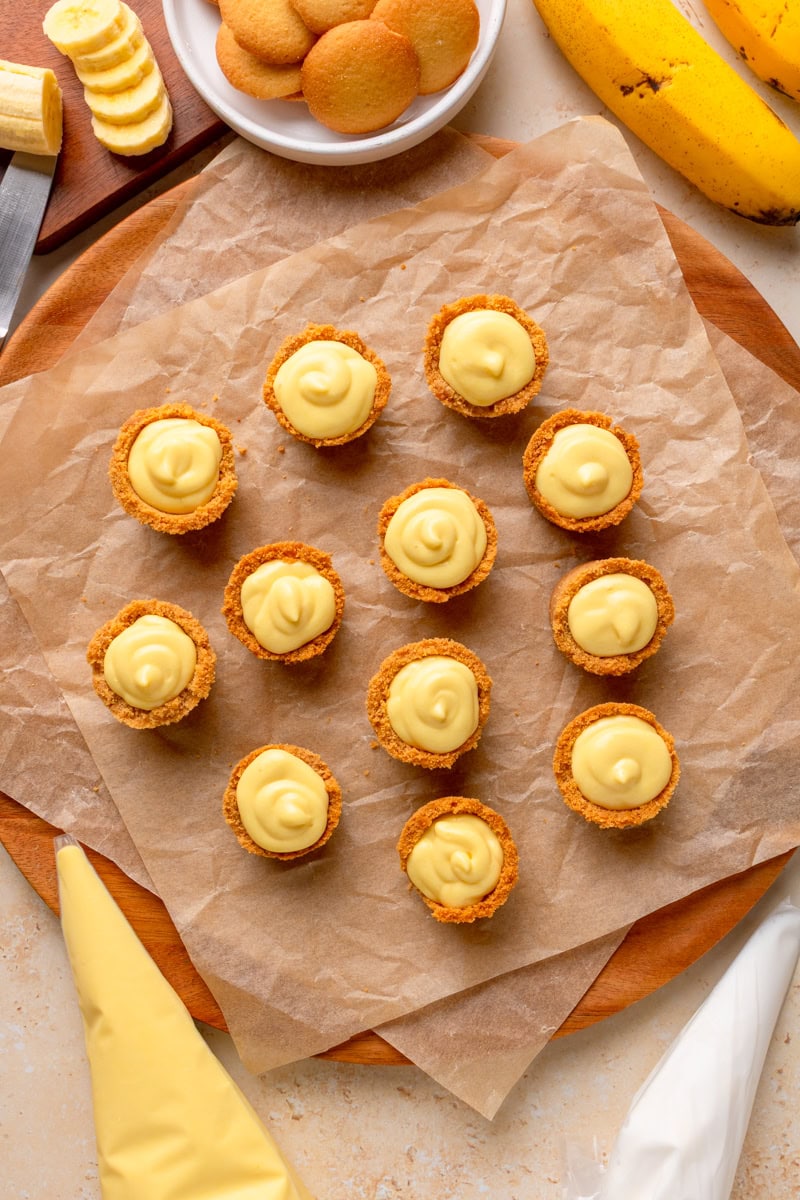 Spoonfuls of banana cream pie filling being added on top of the crusts.