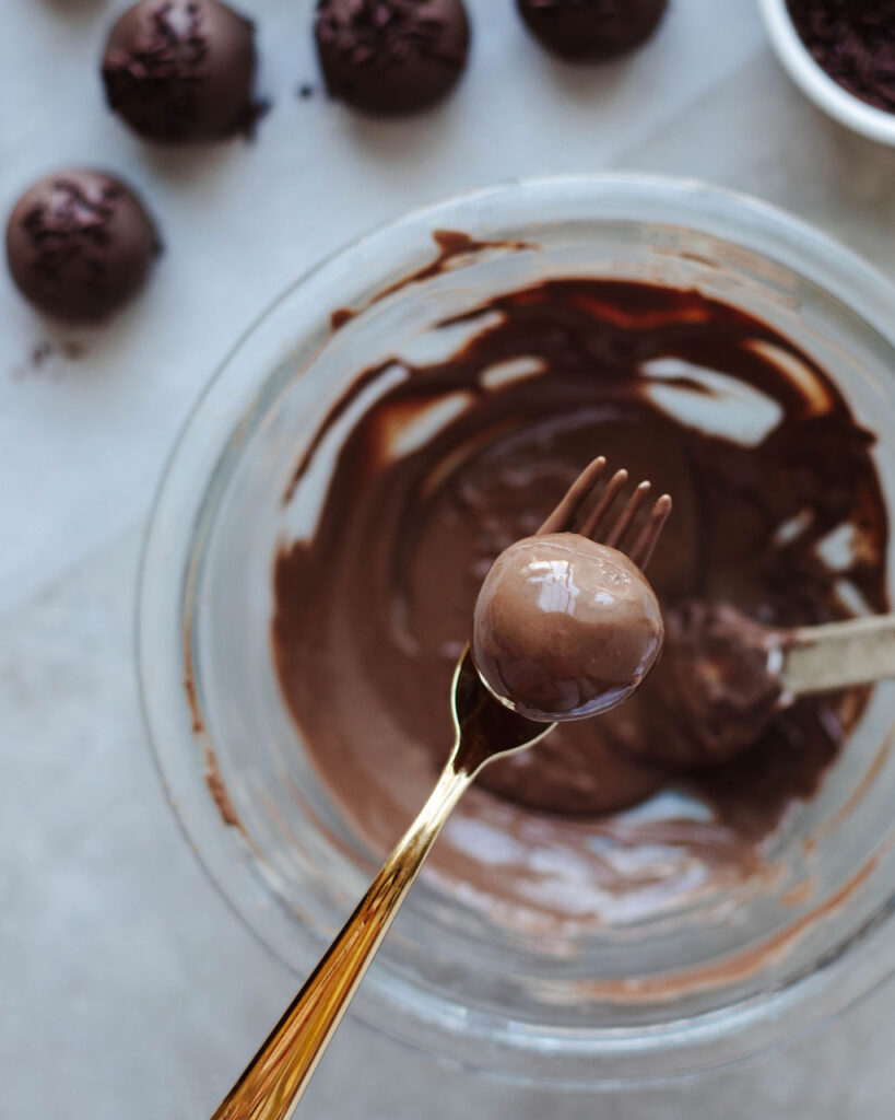 a chocolate cake ball dipped in melted chocolate on a fork.