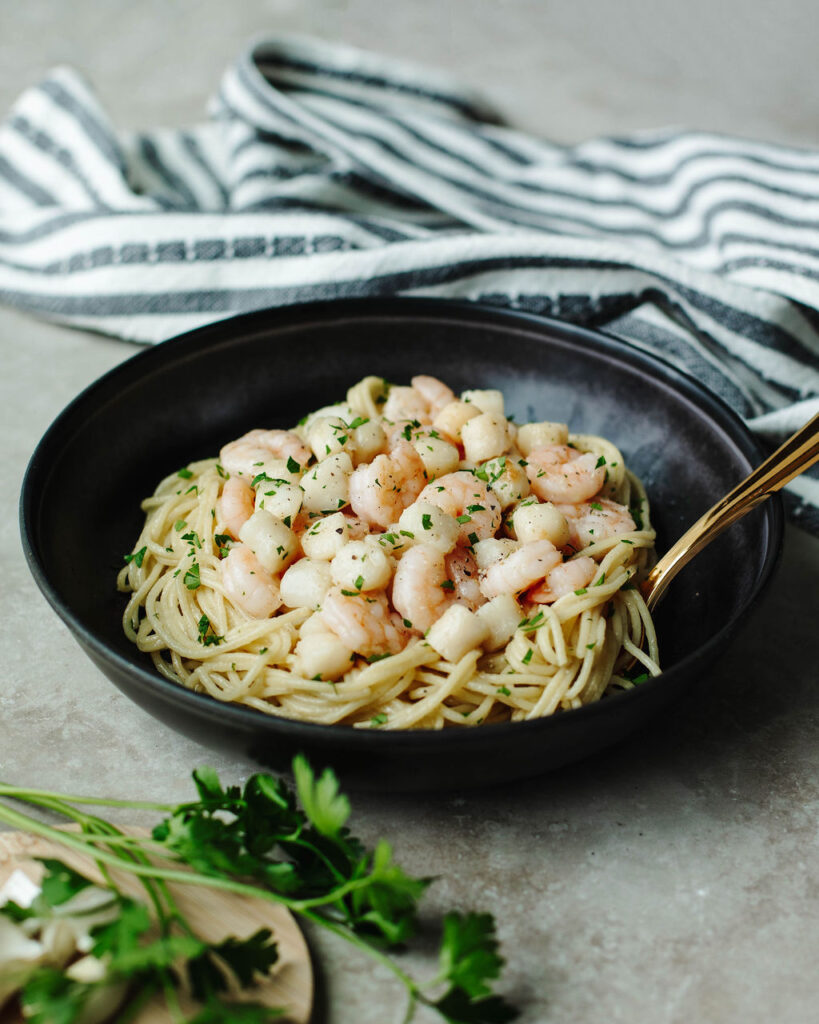 a black serving bowl with Garlic Butter Grilled Shrimp and Scallops over pasta.
