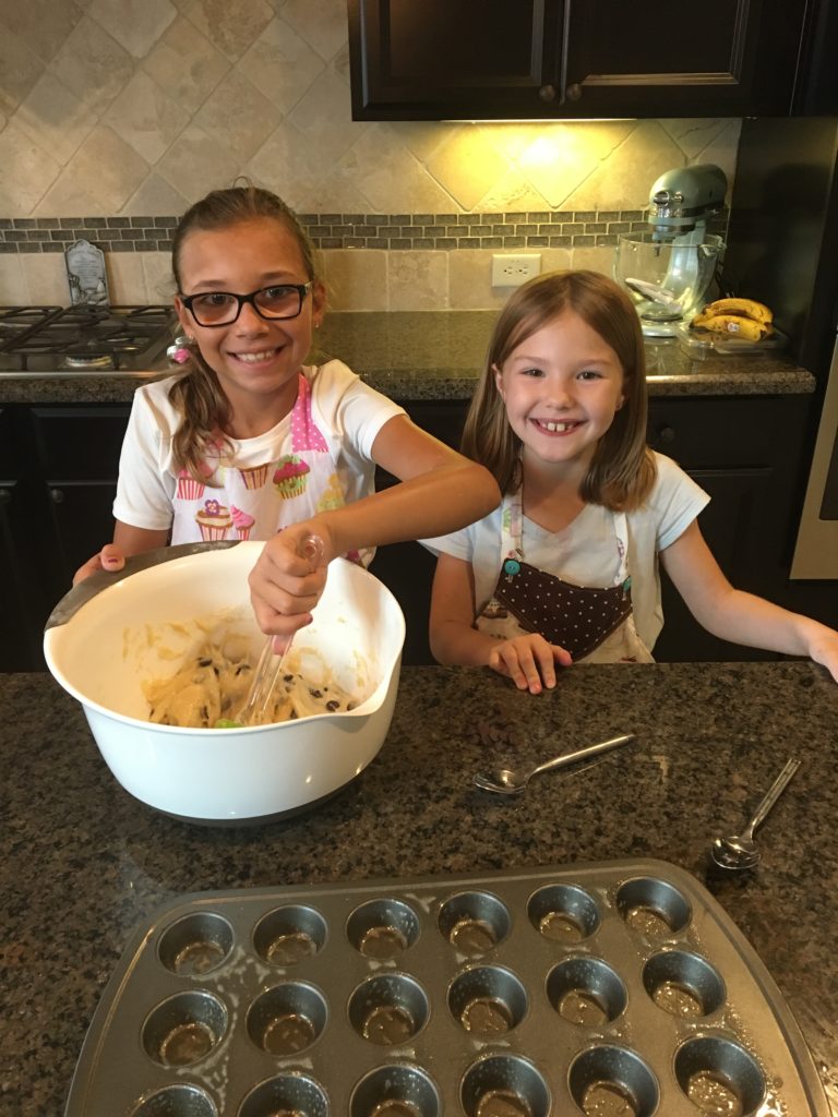 two girls preparing the batter for mini chocolate chip muffins