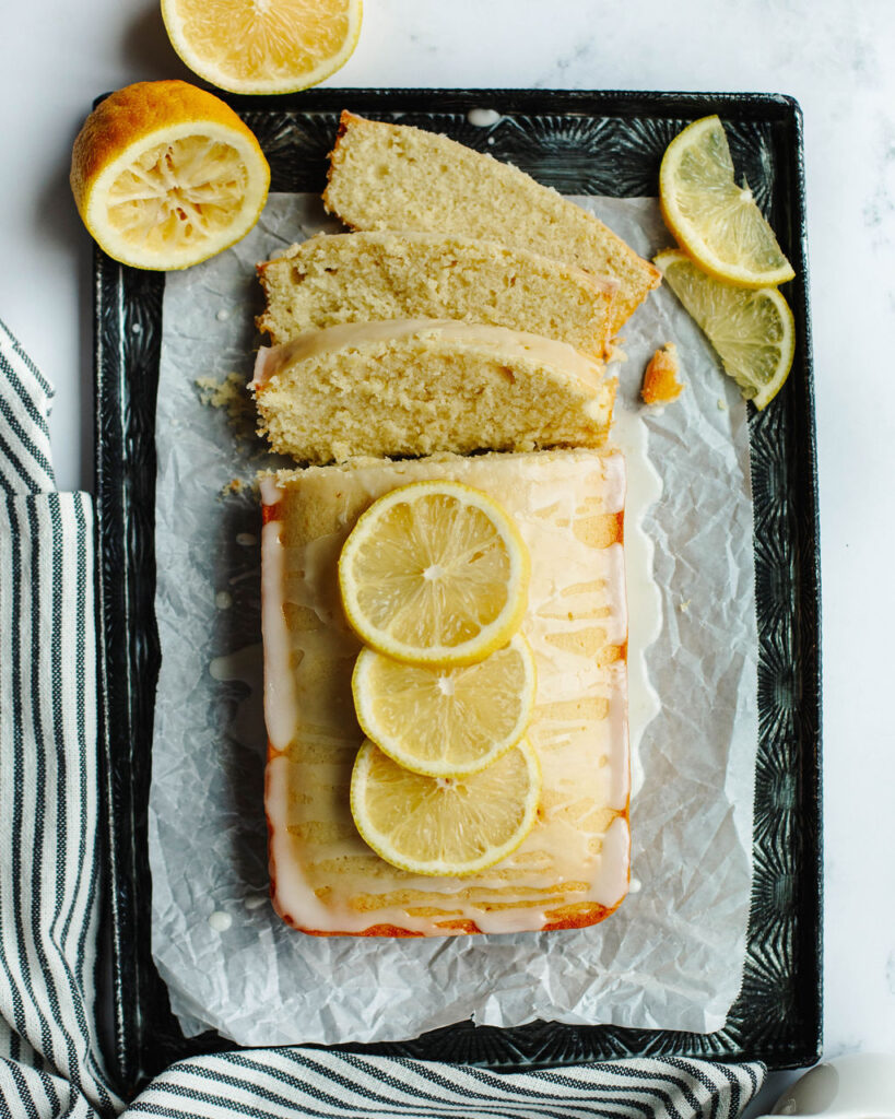 glazed lemon loaf on a piece of parchment paper with lemon wedges.