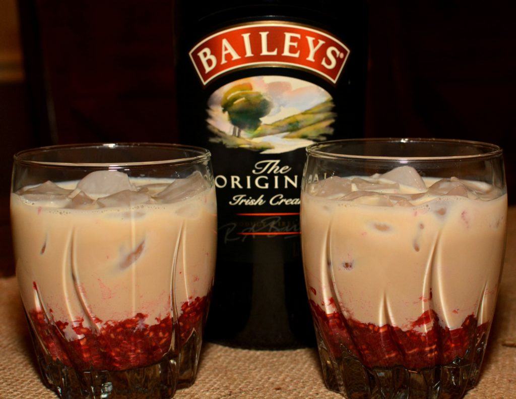 fresh raspberries muddled on the bottom of a glass with baileys irish cream poured over ice
