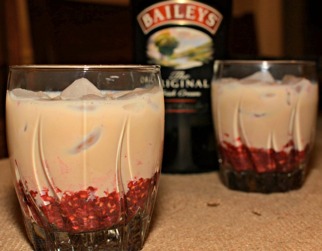 baileys irish cream poured over ice cubes with muddled raspberries to create baileys raspberry cocktails