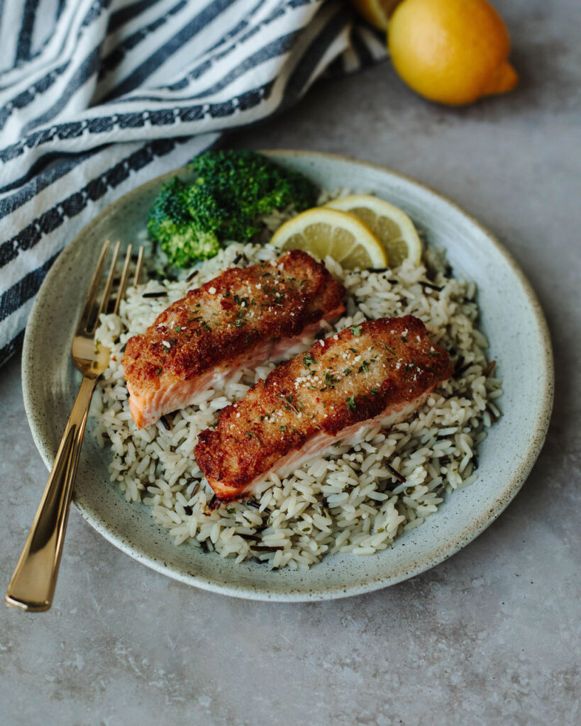 Parmesan Crusted Salmon with a mayo sauce cooked and placed on a white plate with rice.
