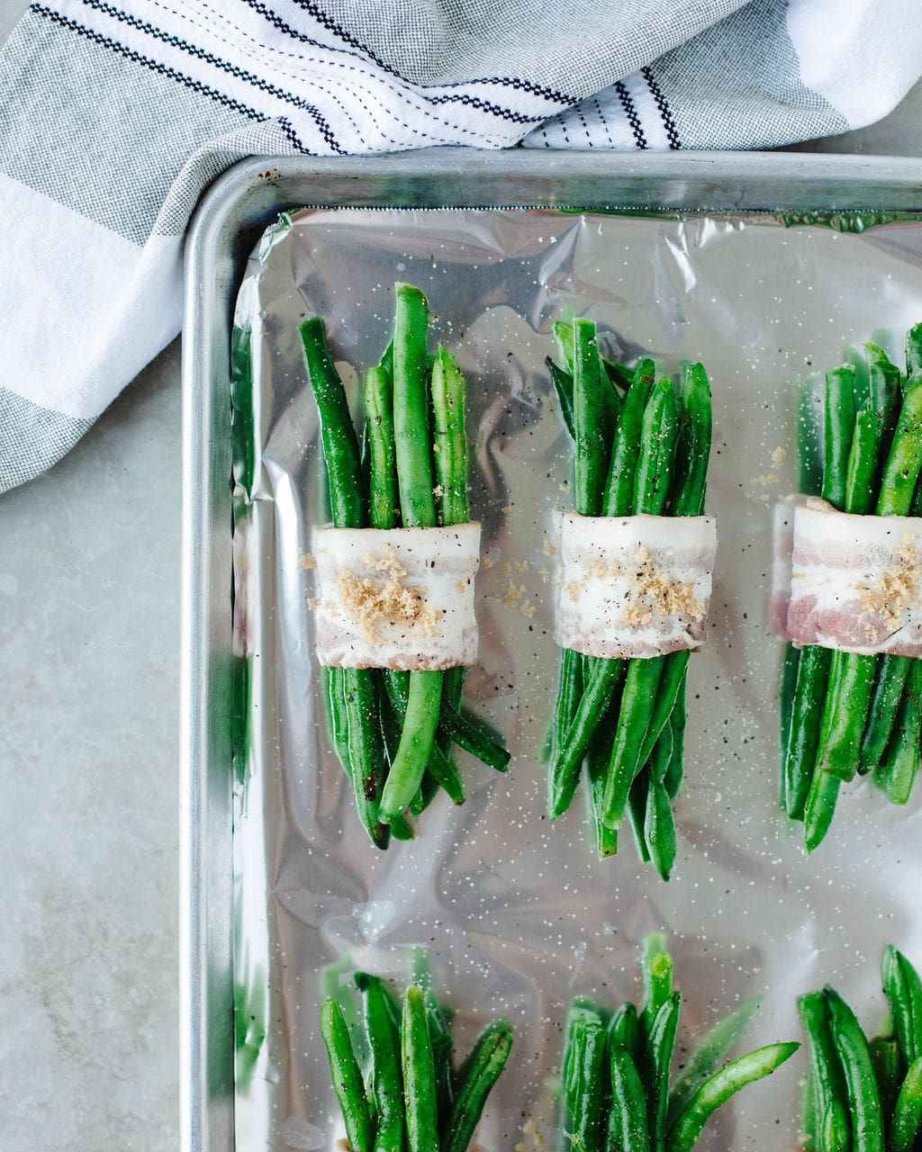 Green bean bundles wrapped in bacon before baking, seasoned with salt, pepper, and brown sugar