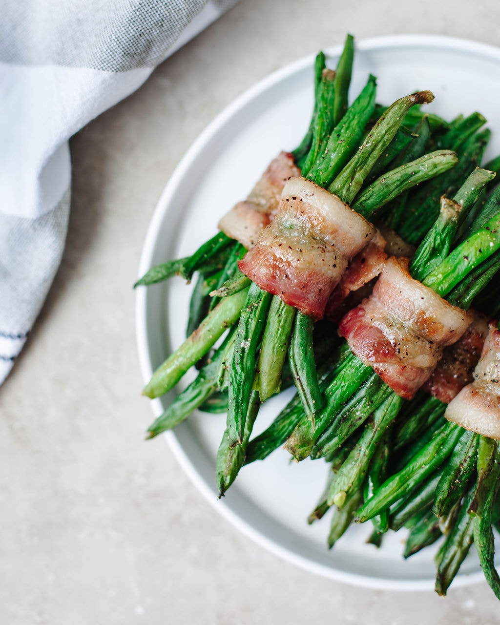 Bacon wrapped green bean bundles fresh out of the oven on a white plate.