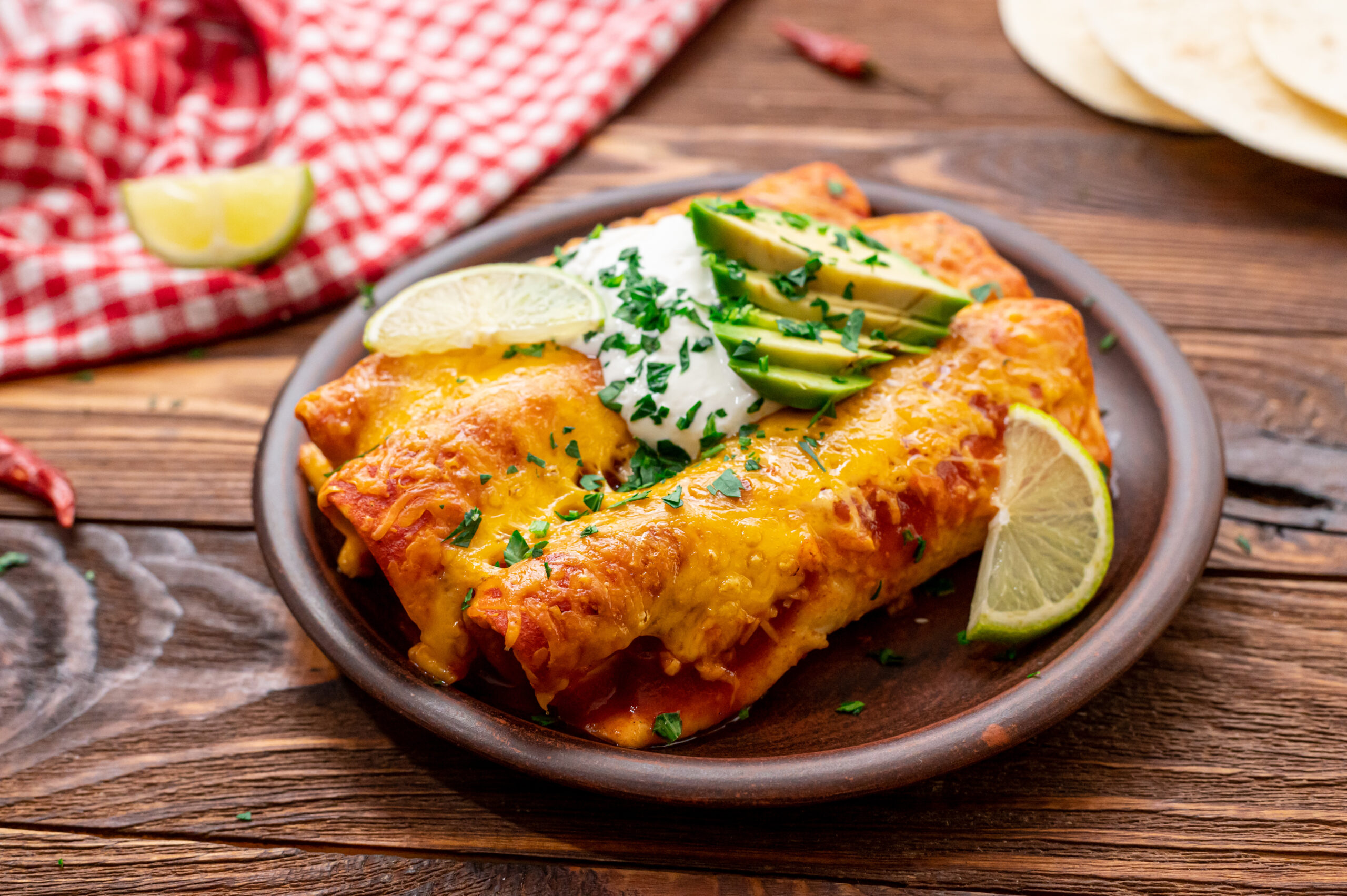 beef enchiladas served with sour cream and avocado slices on top.