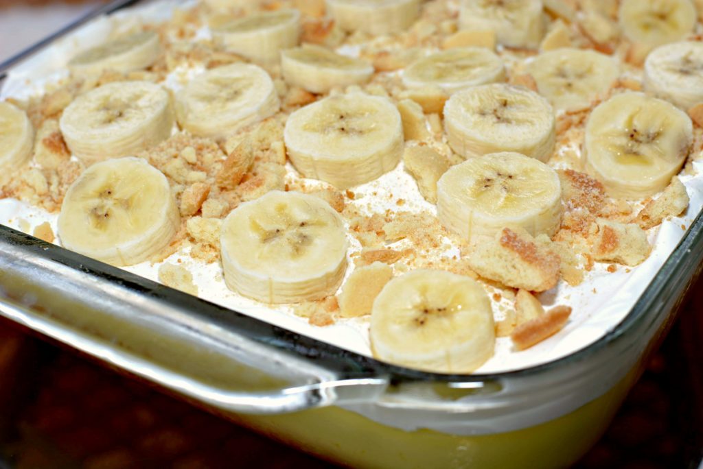 cool whip and bananas top a yellow cake with banana pudding poured into poked holes