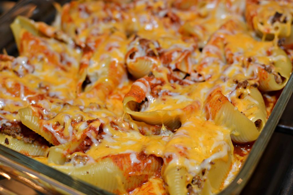 Mexican stuffed shells with seasoned taco meat, enchilada sauce, and shredded cheese served in a casserole dish.