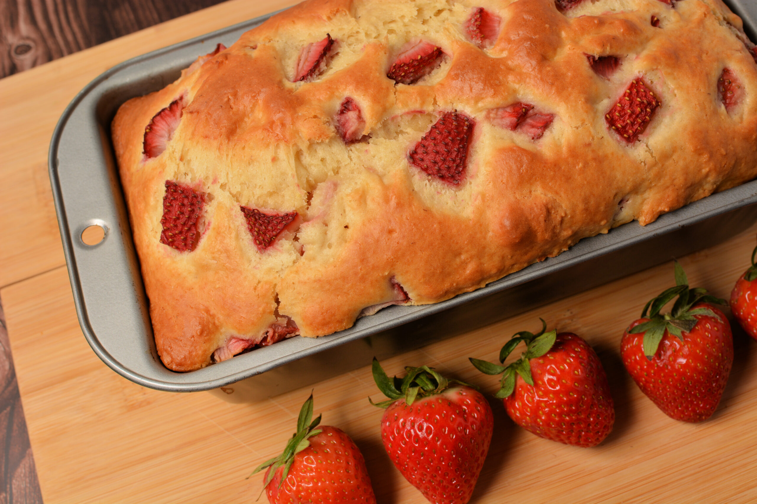 a loaf of strawberry quick bread on a cutting board.
