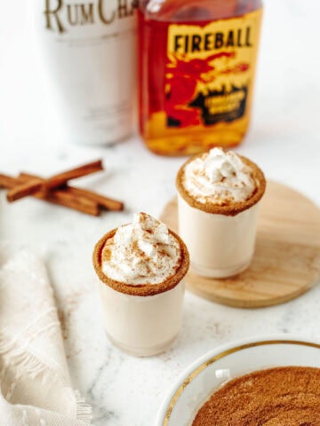 two cinnamon toast crunch shots topped with whipped cream and a cinnamon sugar rim.