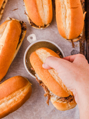 a french dip sandwich getting dipped into au jus