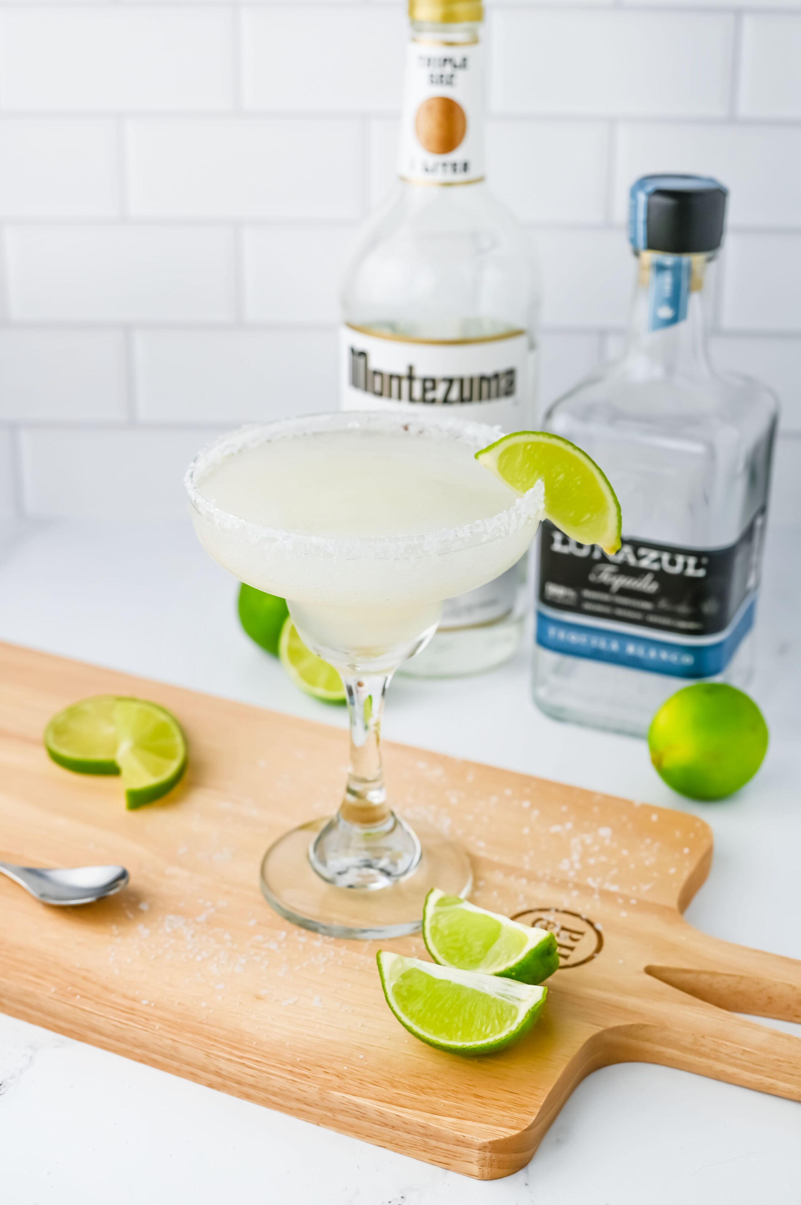 a blended frozen limeade margarita on a wood cutting board with lime slices.