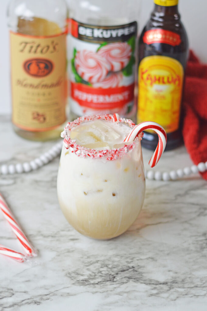 a festive peppermint cocktail in a glass with a candy cane.