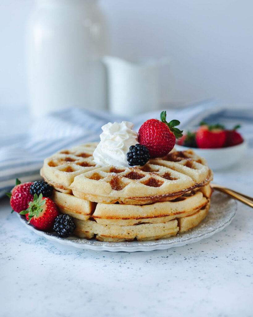 fluffy waffles stacked on a plate with fresh berries.