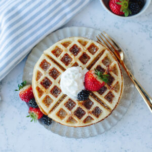 whipped cream and fresh berries topped on homemade waffles on a white plate.