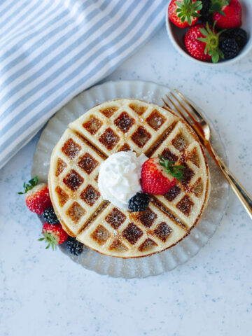 whipped cream and fresh berries topped on homemade waffles on a white plate.