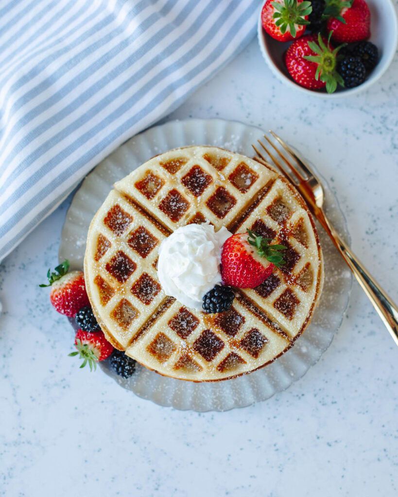 whipped cream and fresh berries topped on homemade waffles on a white plate.