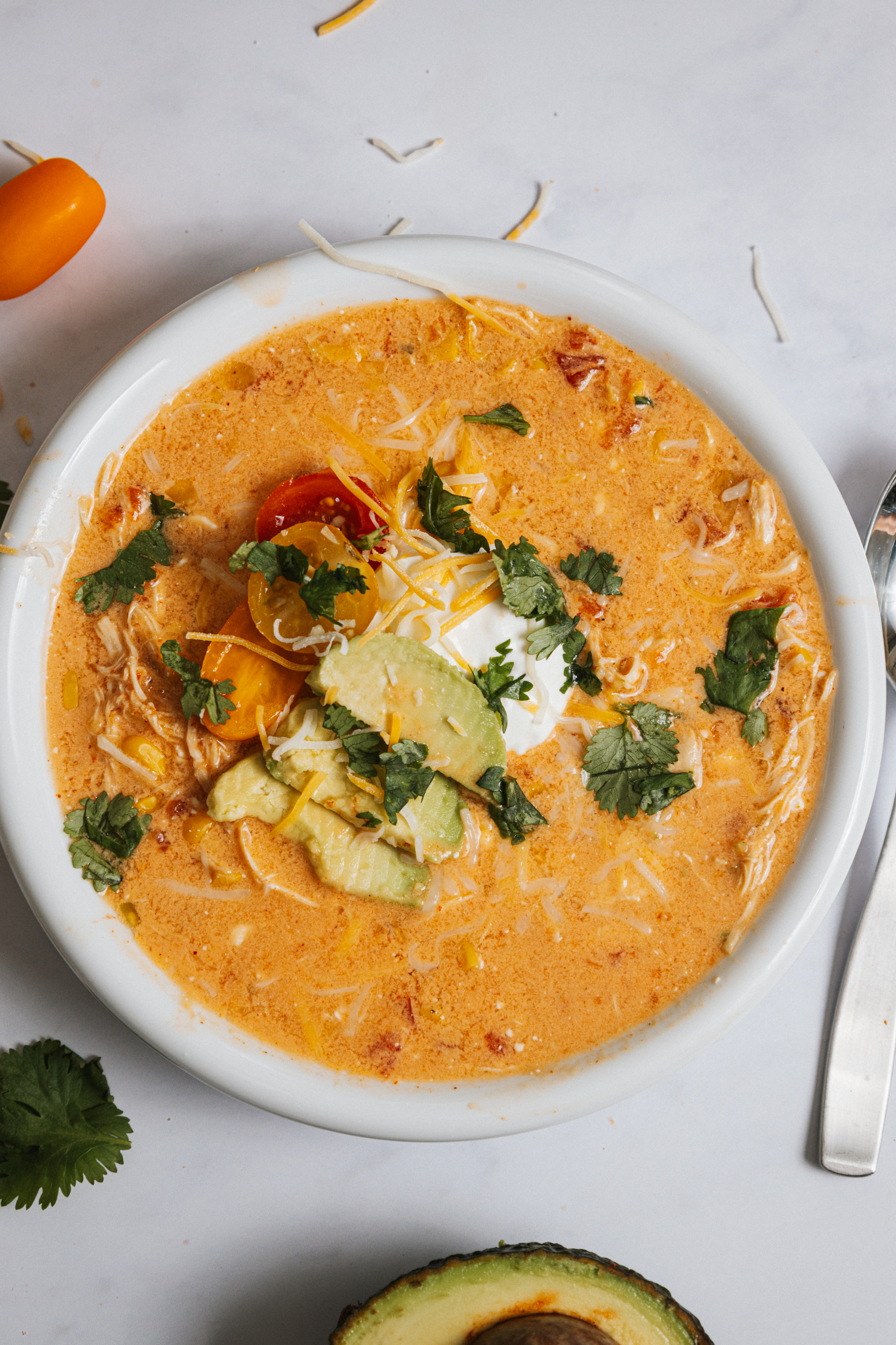 a white bowl of soup with spices and seasonings and topped with sour cream, avocado and cilantro.