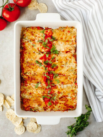 Creamy Shrimp Enchiladas topped with tomatoes in a white baking dish.
