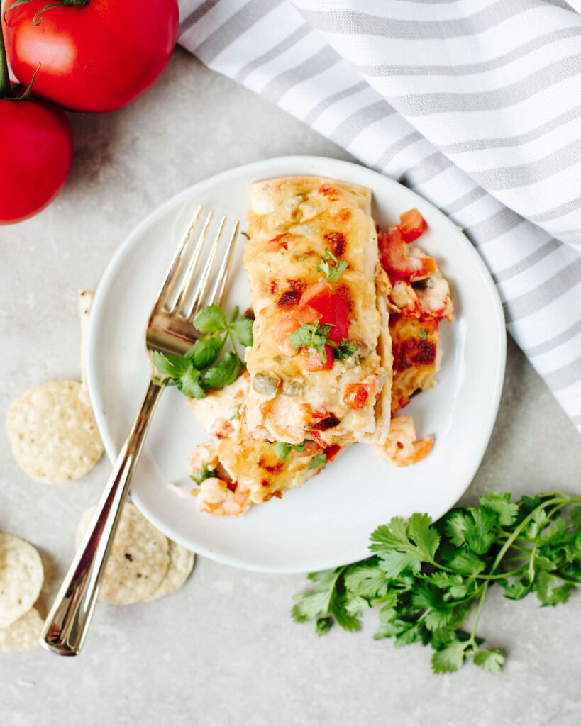 a white dinner plate with two shrimp enchiladas ready to enjoy.