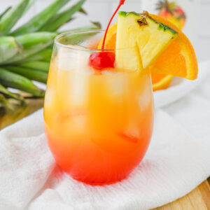 a tropical cocktail in a glass garnished with pineapple and orange wedges.