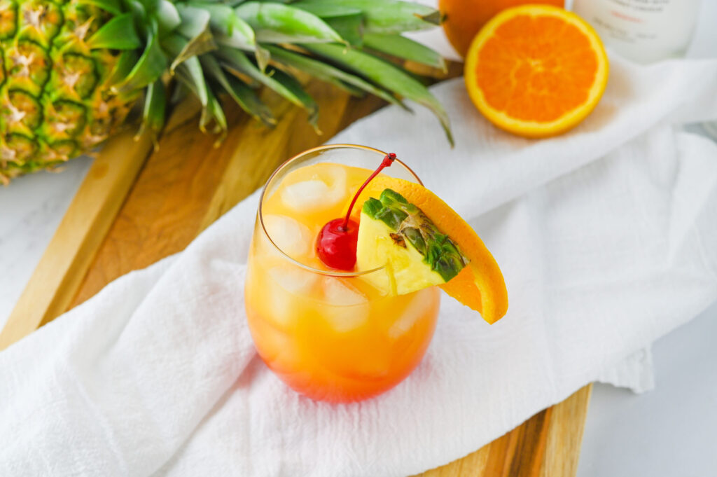 a garnished fruit cocktail served in a cocktail glass with pineapple, orange, and cherries.