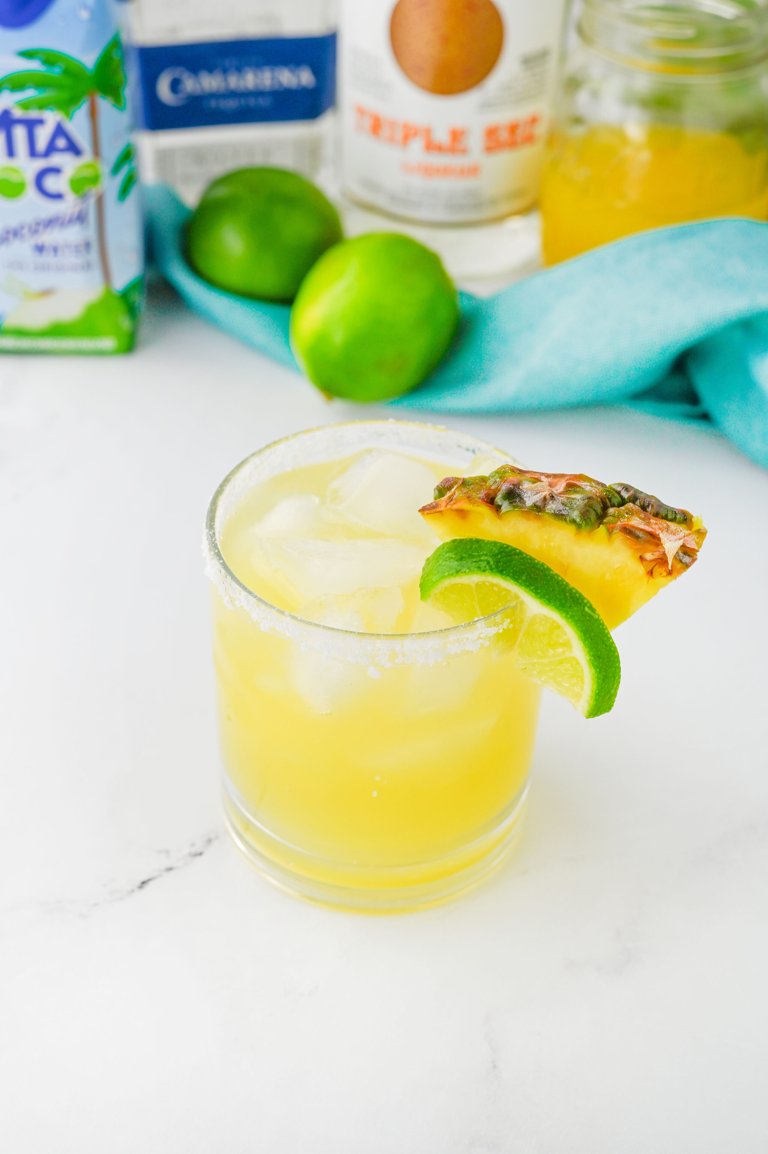 a Hawaiian margarita in a glass with lime wedges and pineapple.