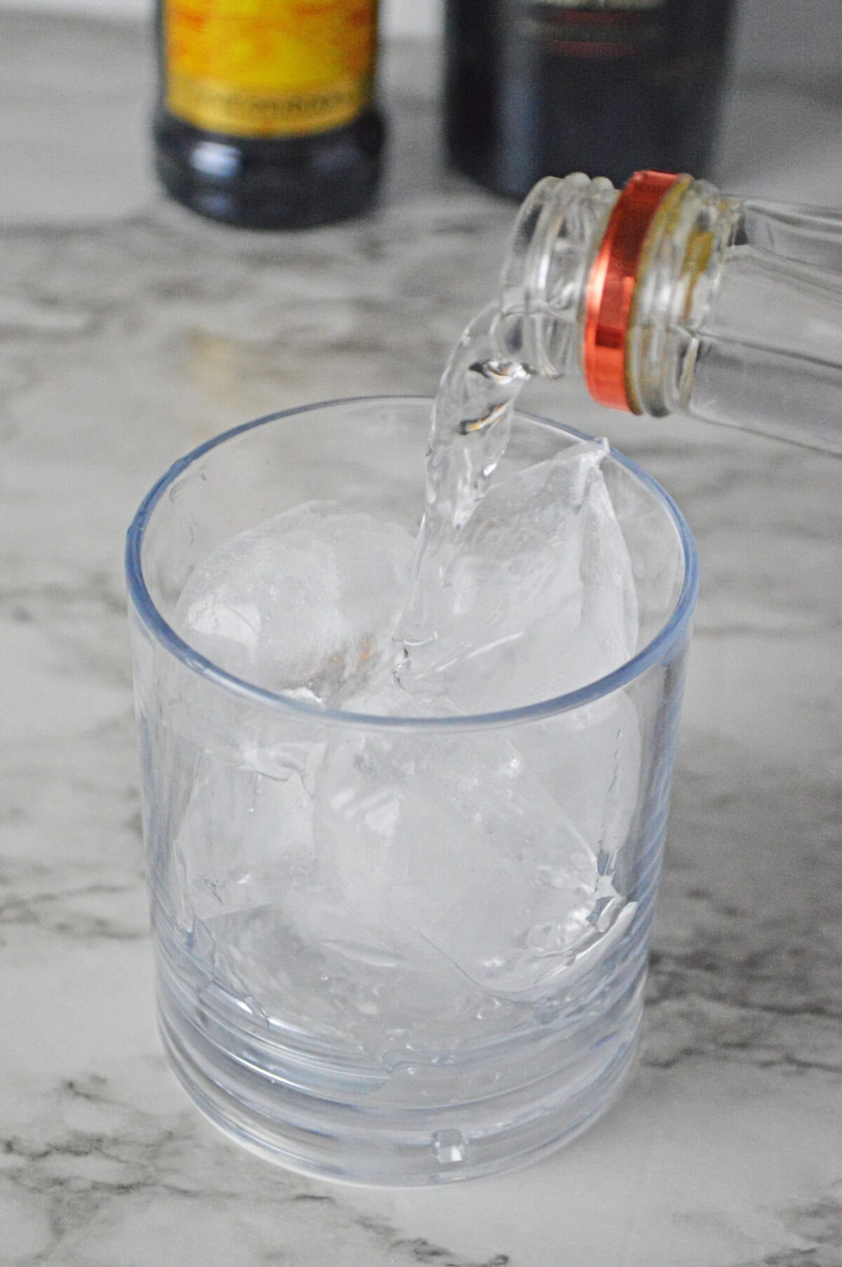 ice cubes added to a rocks glass with vodka.