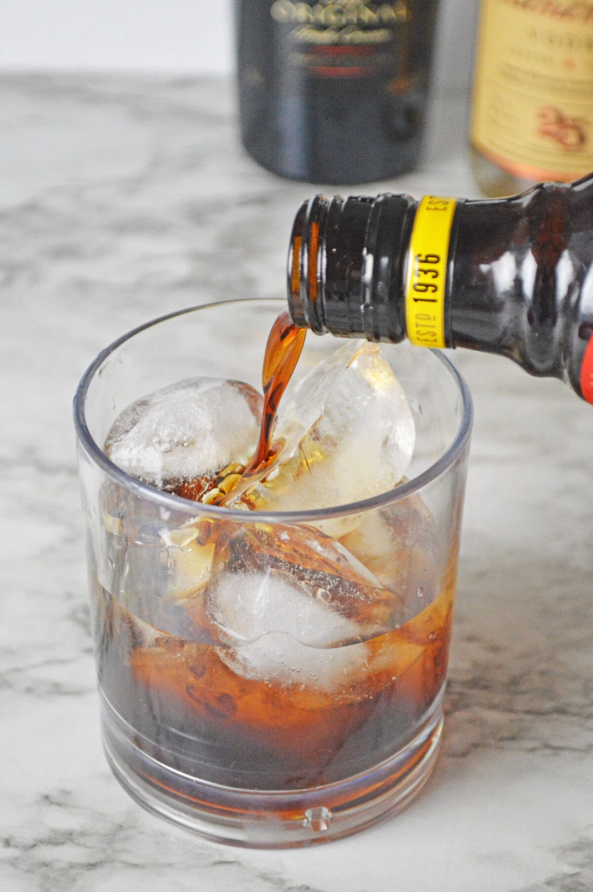 Kahlua being poured over ice and vodka in a glass.